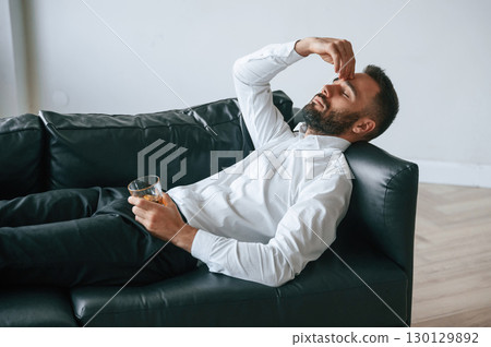 Having headache, lying down on the sofa. Upset young man drinker alcoholic is indoors Having headache, lying down on the sofa. Upset young man drinker alcoholic is indoors 130129892