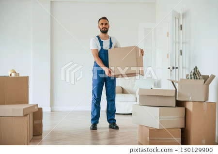 Full height photo, standing and holding big box. Moving service employee in a room 130129900