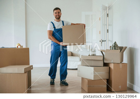 Full height photo, standing and holding big box. Moving service employee in a room Full height photo, standing and holding big box. Moving service employee in a room 130129964
