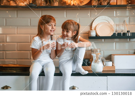 Having fun. Happy two little girls are drinking milk while sitting on the table on the kitchen Having fun. Happy two little girls are drinking milk while sitting on the table on the kitchen 130130018