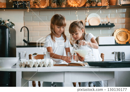 Pouring the milk. Two little girls are preparing food on the kitchen with garlands 130130177