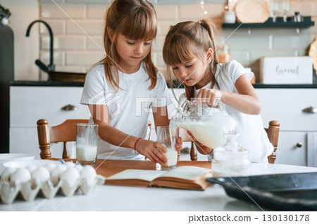 Pouring the milk. Two little girls are preparing food on the kitchen with garlands 130130178