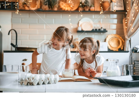With receipt book. Two little girls are preparing food on the kitchen with garlands With receipt book. Two little girls are preparing food on the kitchen with garlands 130130180