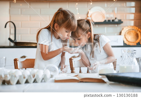 Using flour. Two little girls are preparing food on the kitchen with garlands 130130188