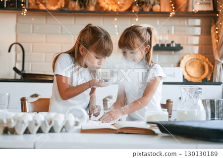 Using flour. Two little girls are preparing food on the kitchen with garlands 130130189