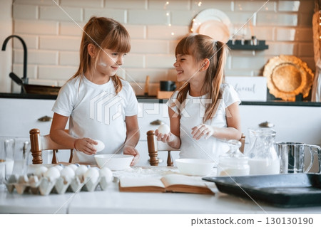 Using flour. Two little girls are preparing food on the kitchen with garlands Using flour. Two little girls are preparing food on the kitchen with garlands 130130190