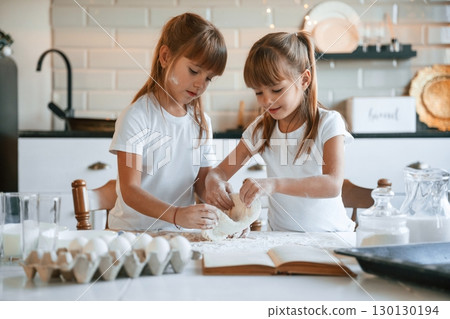 Flour and eggs on the table. Two little girls are preparing food on the kitchen with garlands 130130194