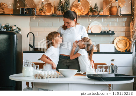 On the kitchen with garlands together. Mother with her little two daughters is preparing food On the kitchen with garlands together. Mother with her little two daughters is preparing food 130130238