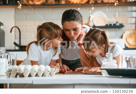 On the kitchen with garlands together. Mother with her little two daughters is preparing food On the kitchen with garlands together. Mother with her little two daughters is preparing food 130130239