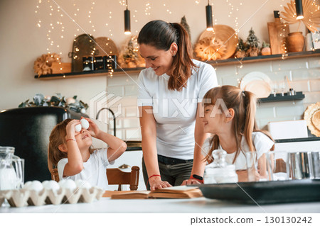 On the kitchen with garlands together. Mother with her little two daughters is preparing food On the kitchen with garlands together. Mother with her little two daughters is preparing food 130130242