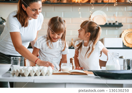 Using quality products. Mother with her little two daughters is preparing food on the kitchen with garlands together 130130250