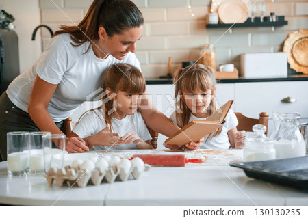 Natural ingredients. Mother with her little two daughters is preparing food on the kitchen with garlands together Natural ingredients. Mother with her little two daughters is preparing food on the kitchen with garlands together 130130255