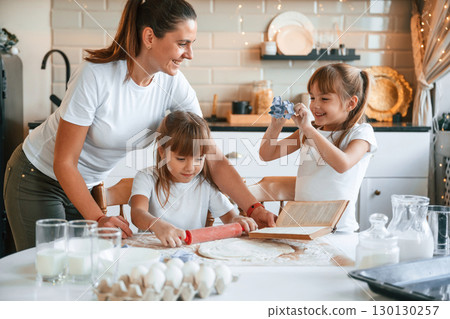 Natural ingredients. Mother with her little two daughters is preparing food on the kitchen with garlands together 130130257