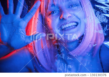 Smiling, positive facial expression. Stylish woman with white hair is behind wet transparent plastic sheet 130130376
