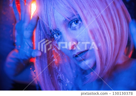 Blue color in the front and red is behind. Stylish woman with white hair is behind wet transparent plastic sheet Blue color in the front and red is behind. Stylish woman with white hair is behind wet transparent plastic sheet 130130378