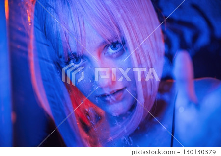 Blue color in the front and red is behind. Stylish woman with white hair is behind wet transparent plastic sheet 130130379