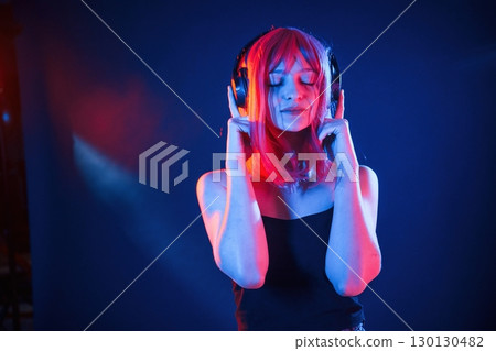 Conception of music, listening in headphones. Woman with white hair is in studio with neon colors Conception of music, listening in headphones. Woman with white hair is in studio with neon colors 130130482