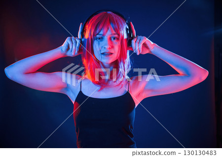 Conception of music, listening in headphones. Woman with white hair is in studio with neon colors 130130483