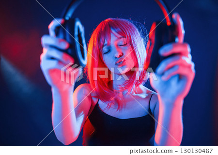 Enjoy the music, holding headphones. Woman with white hair is in studio with neon colors Enjoy the music, holding headphones. Woman with white hair is in studio with neon colors 130130487