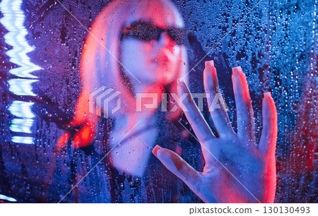 In black sunglasses. Stylish woman with white hair is behind wet transparent plastic sheet In black sunglasses. Stylish woman with white hair is behind wet transparent plastic sheet 130130493