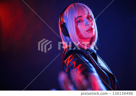 Conception of music, listening in headphones. Woman with white hair is in studio with neon colors Conception of music, listening in headphones. Woman with white hair is in studio with neon colors 130130498