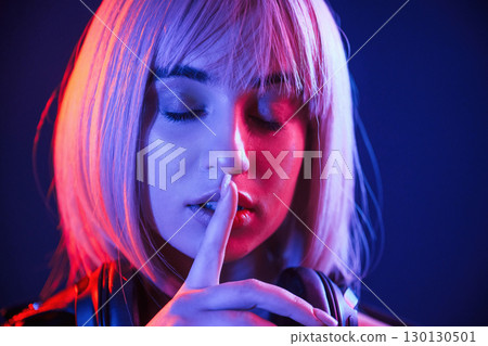 Finger by the lips, silence. Woman with white hair is in studio with neon colors Finger by the lips, silence. Woman with white hair is in studio with neon colors 130130501