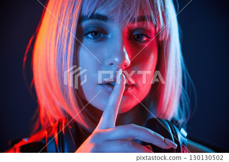 Gesture of be quiet, finger is by the lips. Woman with white hair is in studio with neon colors Gesture of be quiet, finger is by the lips. Woman with white hair is in studio with neon colors 130130502
