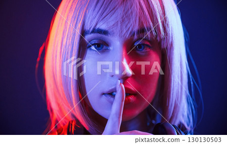 Gesture of be quiet, finger is by the lips. Woman with white hair is in studio with neon colors 130130503