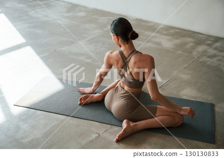 Conception of wellbeing and health care. Rear view of young woman on yoga mat indoors 130130833
