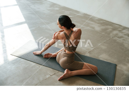 Conception of wellbeing and health care. Rear view of young woman on yoga mat indoors 130130835