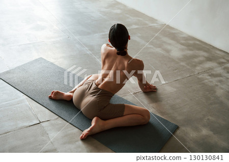 Sitting on yoga mat. Back view of sporty woman that is without bra indoors Sitting on yoga mat. Back view of sporty woman that is without bra indoors 130130841