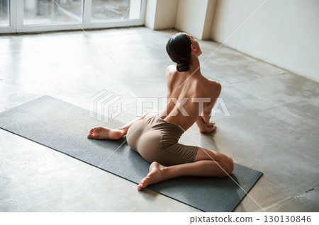 Sitting on yoga mat. Back view of sporty woman that is without bra indoors Sitting on yoga mat. Back view of sporty woman that is without bra indoors 130130846