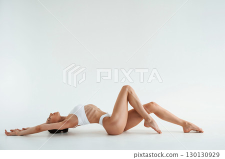 Lying down on the floor. Woman in white underwear with slim body type against white background Lying down on the floor. Woman in white underwear with slim body type against white background 130130929