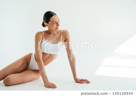 Posing for the camera. Woman in white underwear with slim body type against white background 130130934