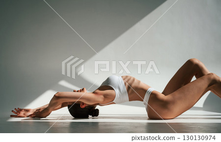 Shadows and sunlight. Doing exercises. Woman in white underwear with slim body type 130130974