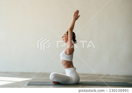 Lotus pose, with hands up. Fitness woman is indoors in white clothes Lotus pose, with hands up. Fitness woman is indoors in white clothes 130130991