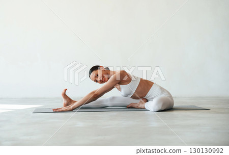 Stretching the legs. Fitness woman is indoors in white clothes Stretching the legs. Fitness woman is indoors in white clothes 130130992