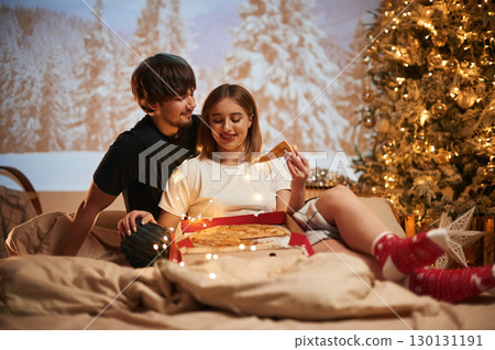 Delicious pizza. Beautiful young couple indoors, celebrating new year against projector 130131191