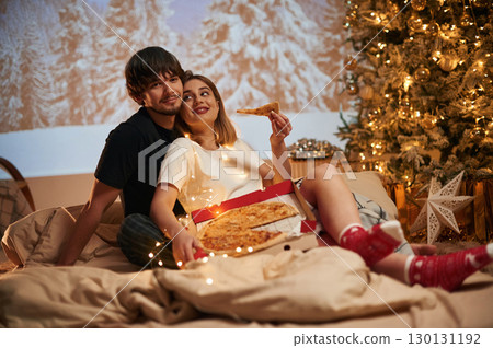 Delicious pizza. Beautiful young couple indoors, celebrating new year against projector 130131192