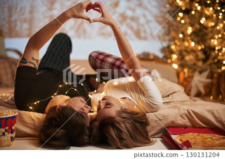 Making love hands gesture. Beautiful young couple indoors, celebrating new year against projector 130131204