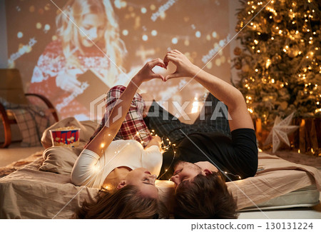 Love gesture by hands. Beautiful young couple indoors, celebrating new year against projector Love gesture by hands. Beautiful young couple indoors, celebrating new year against projector 130131224