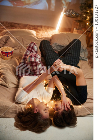 Taking rest, lying down on bed. Beautiful young couple indoors, celebrating new year against projector Taking rest, lying down on bed. Beautiful young couple indoors, celebrating new year against projector 130131227