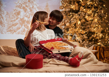 Embracing each other. Beautiful young couple indoors, celebrating new year against projector 130131253
