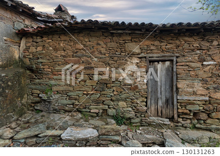 Rustic Stone Wall with Weathered Wooden Door and Traditional Tiled Roof. Old Village House Rustic Stone Wall with Weathered Wooden Door and Traditional Tiled Roof. Old Village House 130131263