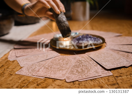 Practicing tarot card reading with crystals and incense in a cozy indoor setting during evening hours Practicing tarot card reading with crystals and incense in a cozy indoor setting during evening hours 130131387