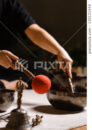 Practicing sound healing with singing bowls during a meditative session at a serene indoor setting with soft lighting 130131434