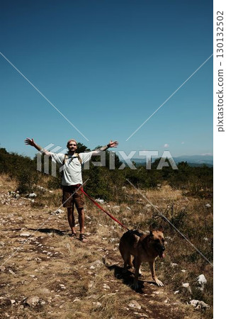 Man raising arms in joy with German Shepherd on hiking trail in Stara Planina, Serbia, surrounded by summer mountains Man raising arms in joy with German Shepherd on hiking trail in Stara Planina, Serbia, surrounded by summer mountains 130132502