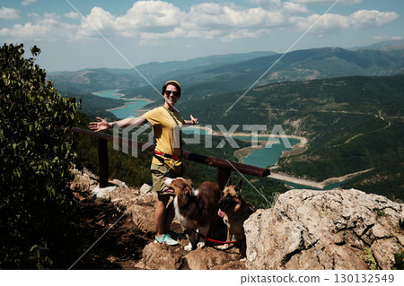 Woman spreading arms in joy with dogs German and Australian Shepherd on mountain viewpoint, stunning turquoise river winding through valley below. Travel and hiking with pets concept. Woman spreading arms in joy with dogs German and Australian Shepherd on mountain viewpoint, stunning turquoise river winding through valley below. Travel and hiking with pets concept. 130132549