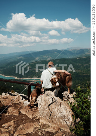 Man sitting on rock with two dogs German and Australian Shepherd overlooking stunning mountain valley and turquoise lake in Stara Planina, Serbia. Travel and hiking with pets concept Man sitting on rock with two dogs German and Australian Shepherd overlooking stunning mountain valley and turquoise lake in Stara Planina, Serbia. Travel and hiking with pets concept 130132556