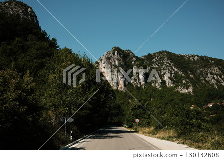 Asphalt road surrounded by forest leading towards rocky mountain cliffs in Stara Planina, Serbia country 130132608